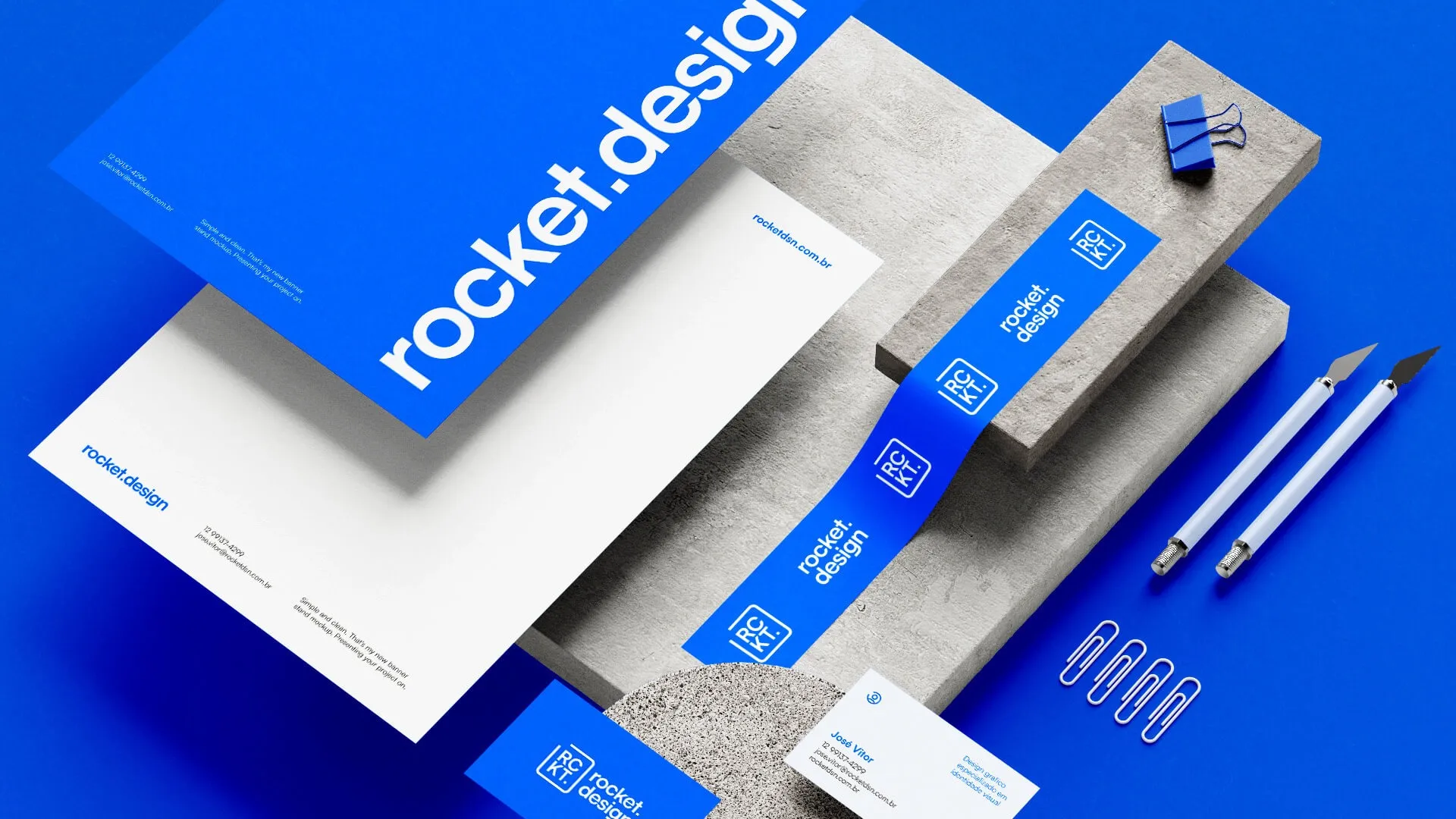 Identidade visual da marca rocket.design com papelaria corporativa em fundo azul, mostrando cartões de visita, papel timbrado e materiais de escritório